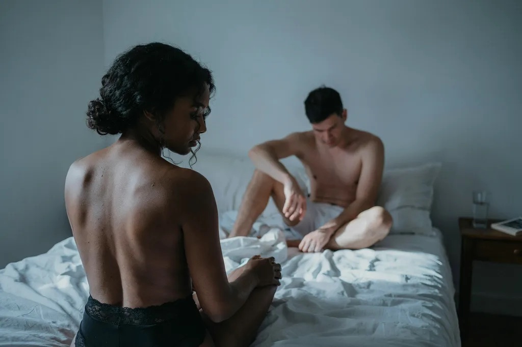 A couple in underwear sitting apart on a bed in soft light