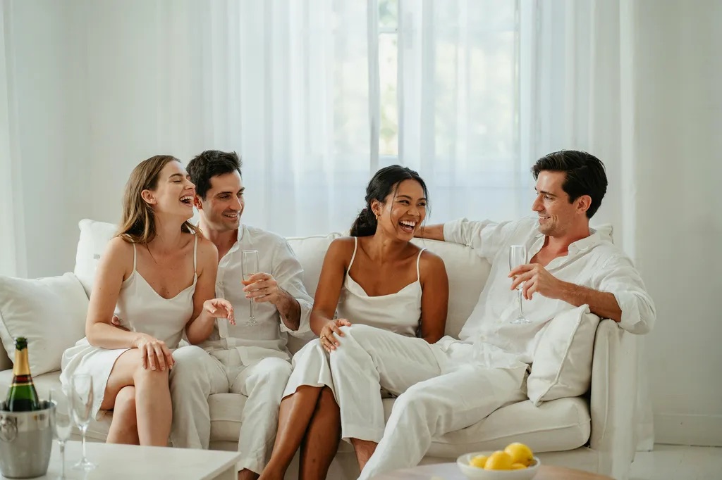 Two couples relaxed together on a white sofa with drinks