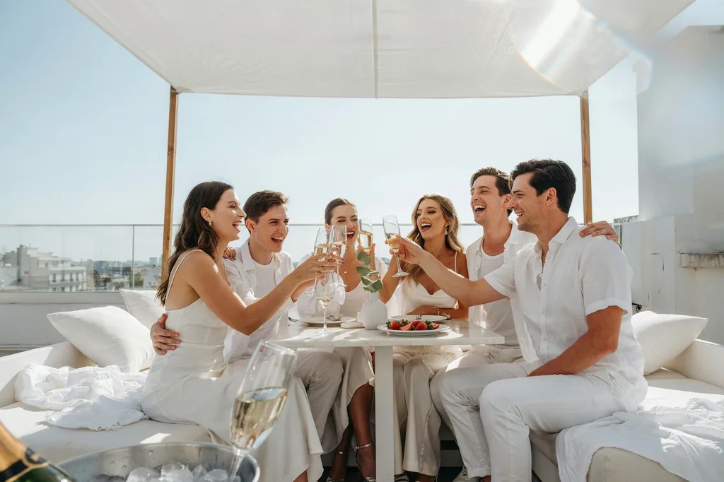 Friends in white raising a toast on a bright rooftop
