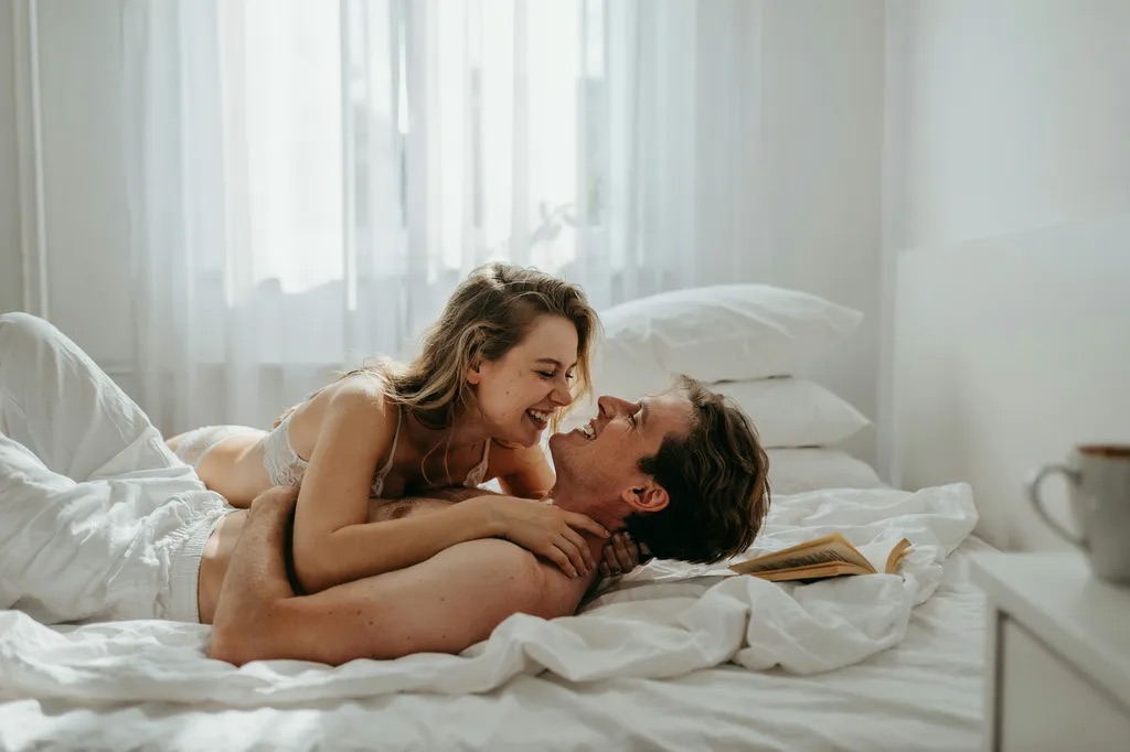 A couple laughing together on a white linen bed in the morning