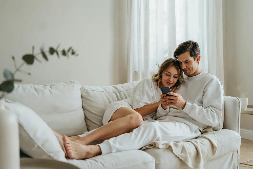A couple at home in white loungewear looking at one phone together